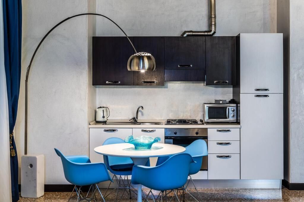 A modern kitchen with a round table, blue chairs, a microwave, and a gas stove.