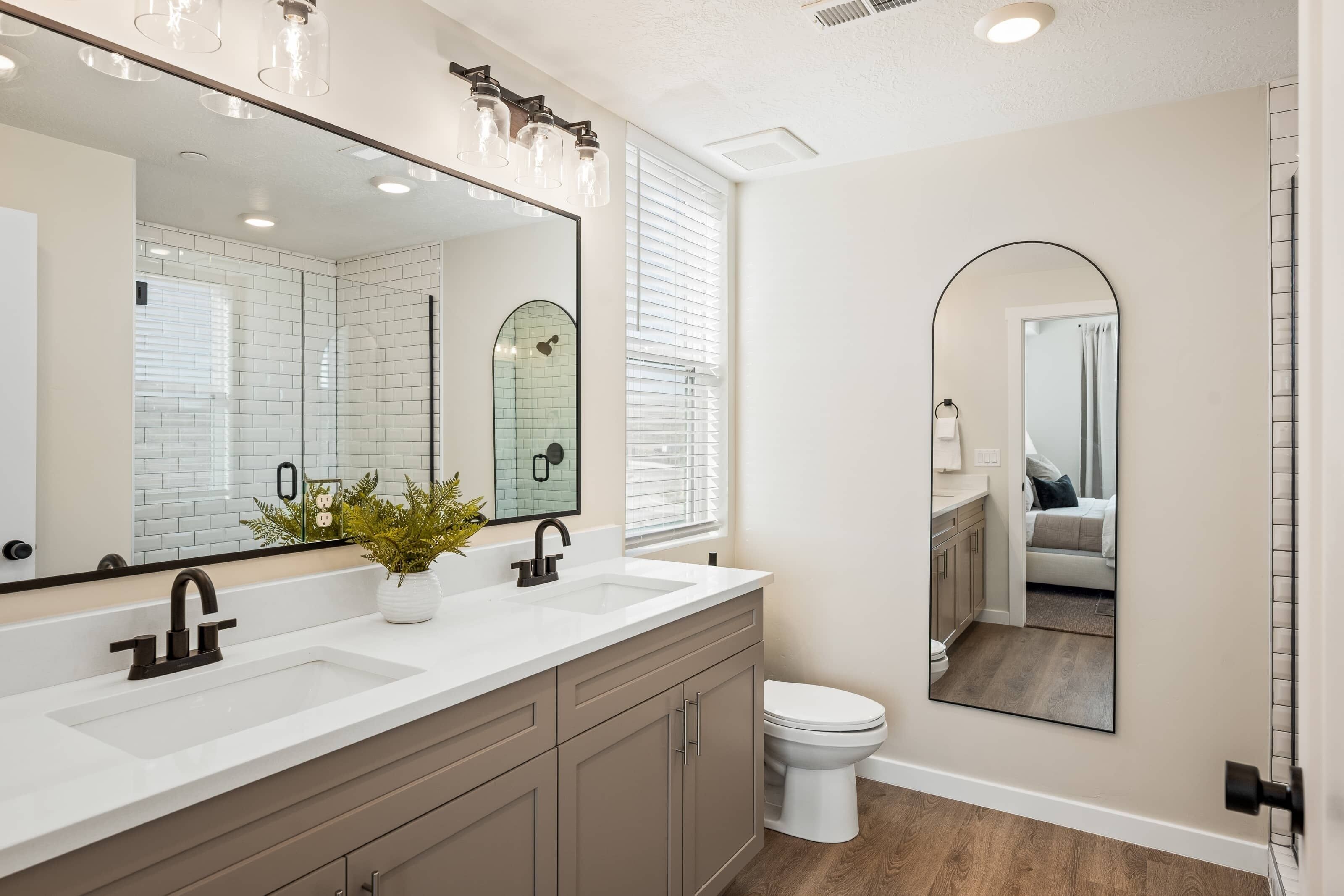 Une salle de bain moderne avec un grand miroir, deux lavabos et des toilettes.
