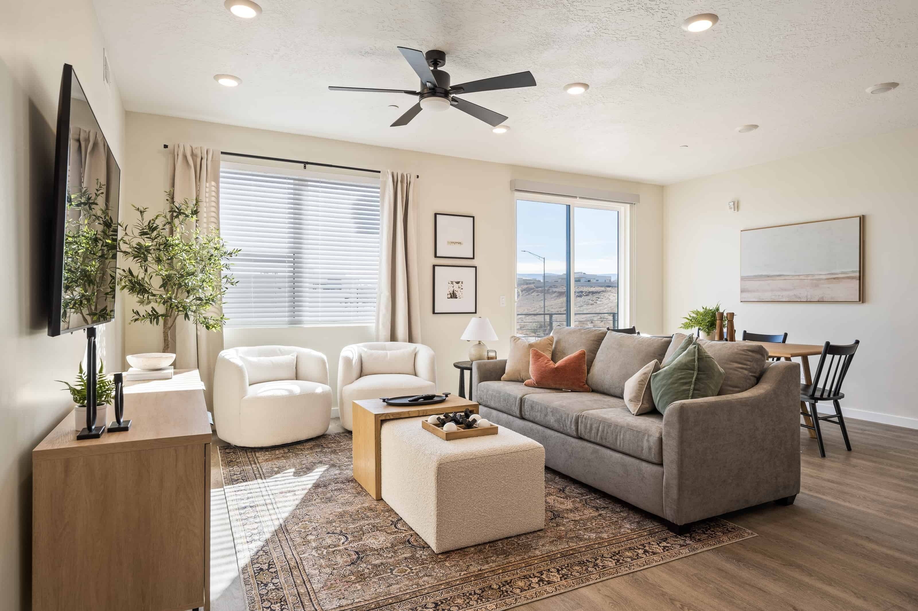 A living room with a sofa, armchairs, a coffee table, a TV, and a ceiling fan.