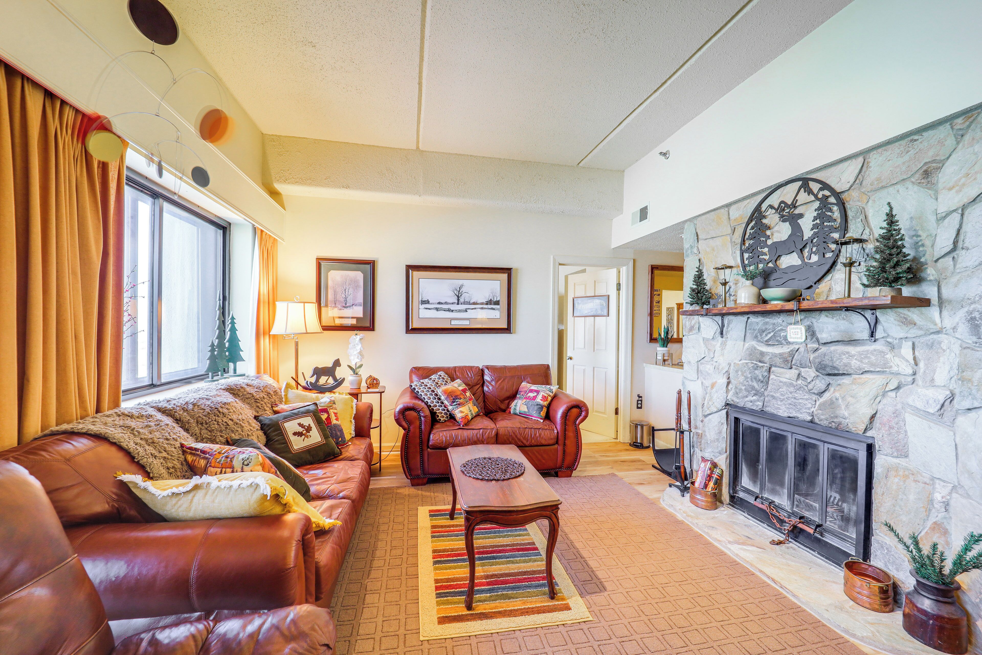 A cozy living room with a stone fireplace, leather sofas, and a large window with curtains.