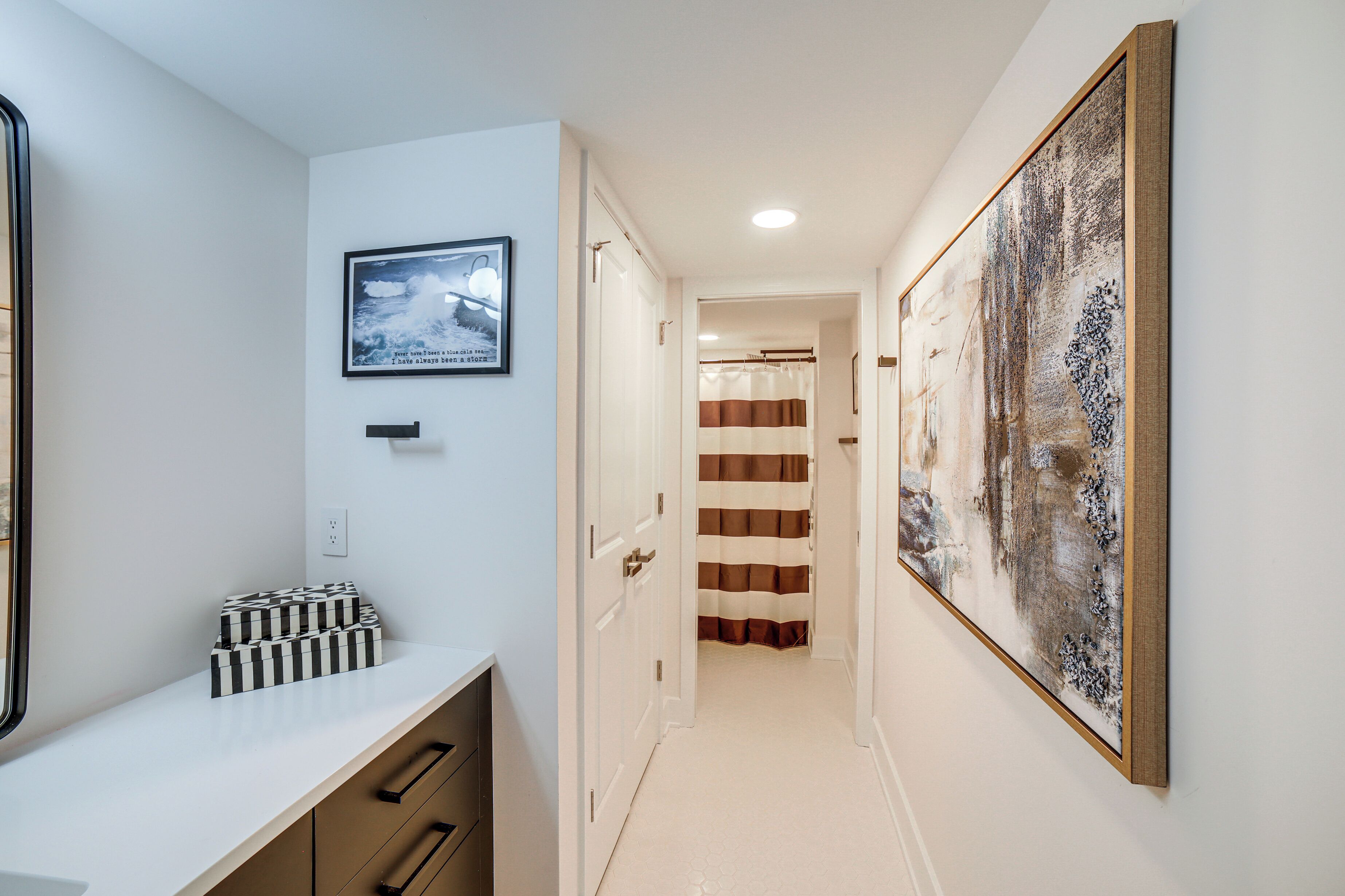 A hallway with a white wall, a framed picture, a white counter with drawers, and a door leading to another room.