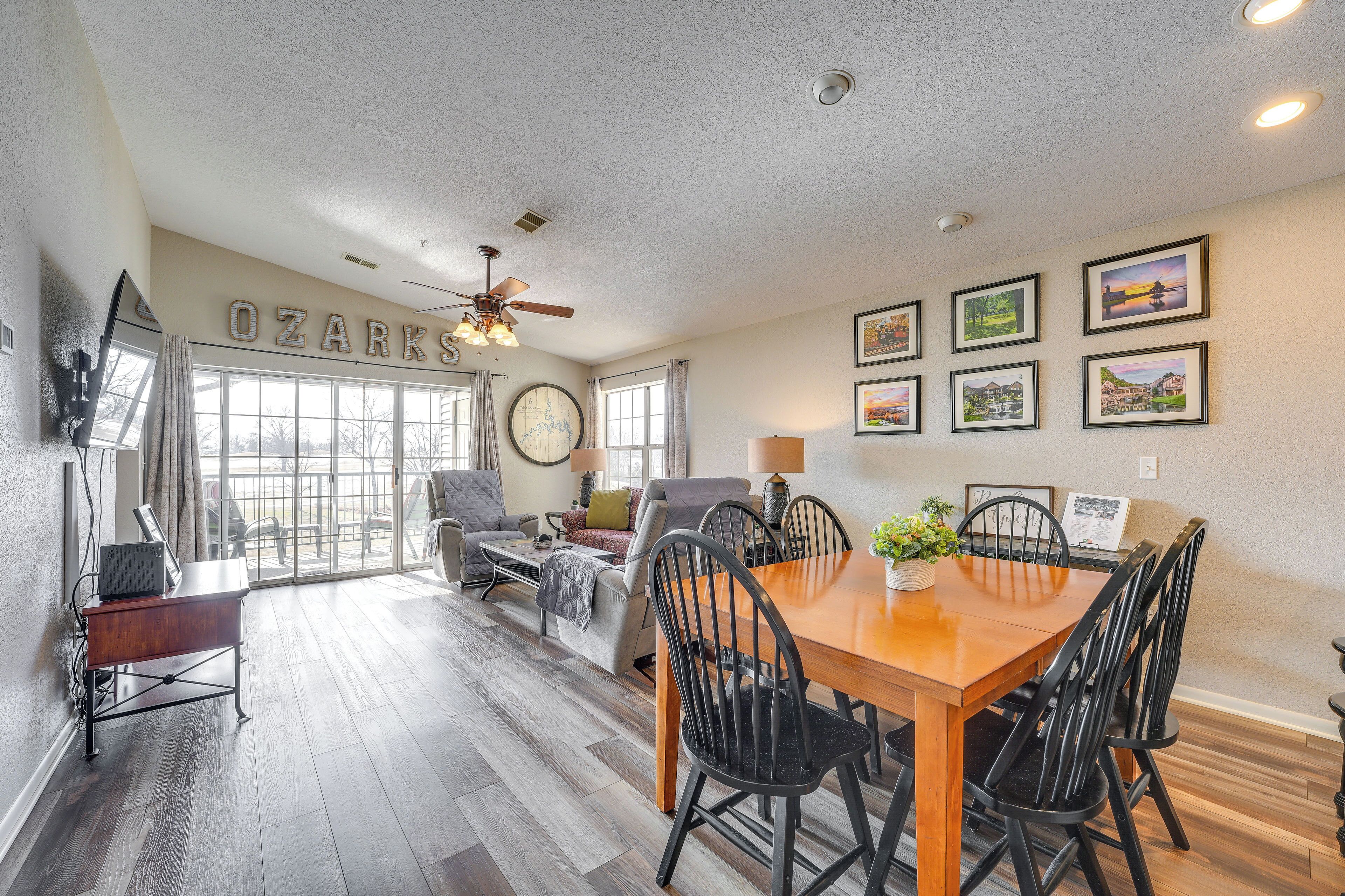 A spacious dining area with a wooden table and chairs, a ceiling fan, and a large window with curtains.
