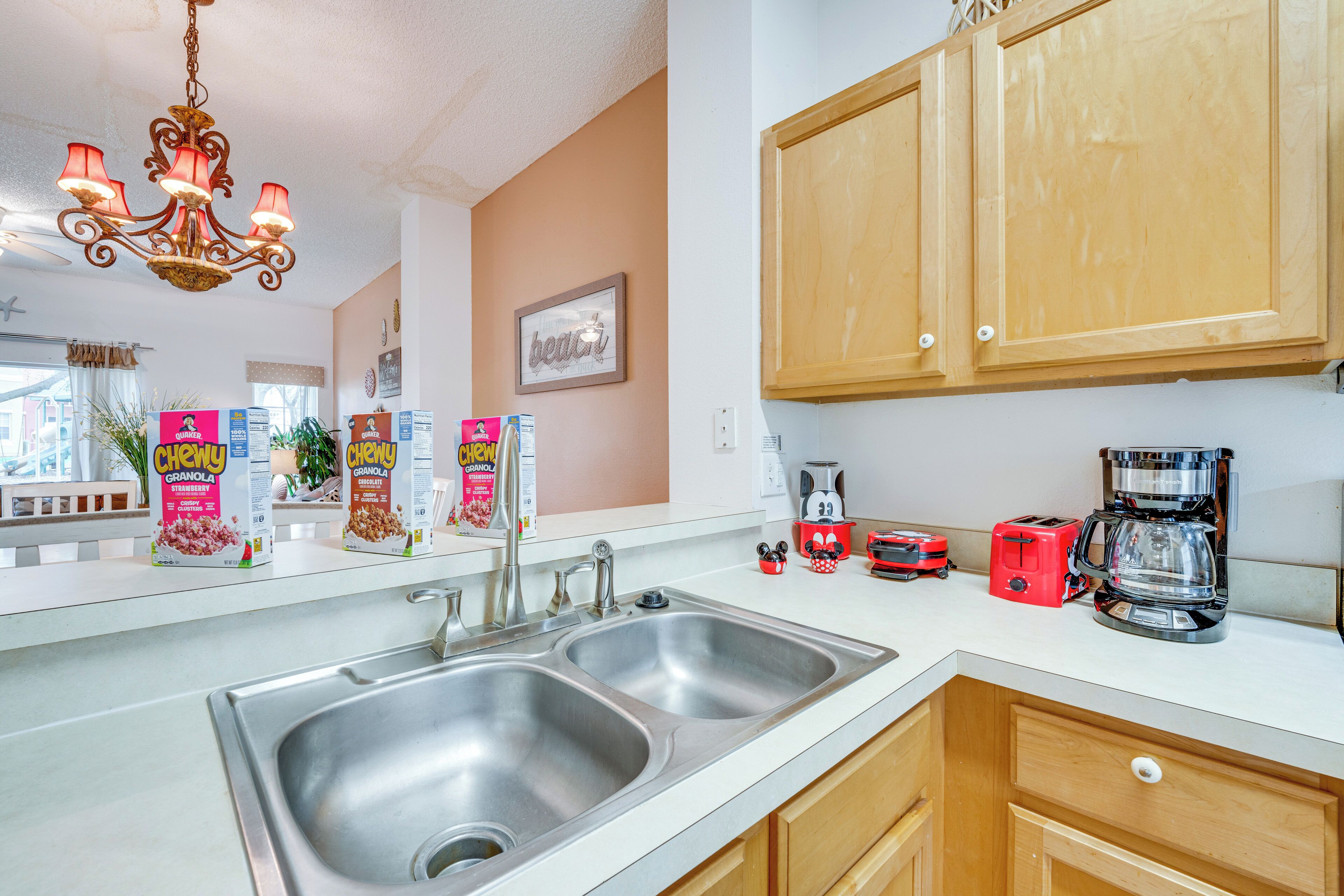 A kitchen with two stainless steel sinks, wooden cabinets, a chandelier, and various appliances including a coffee maker and toaster.