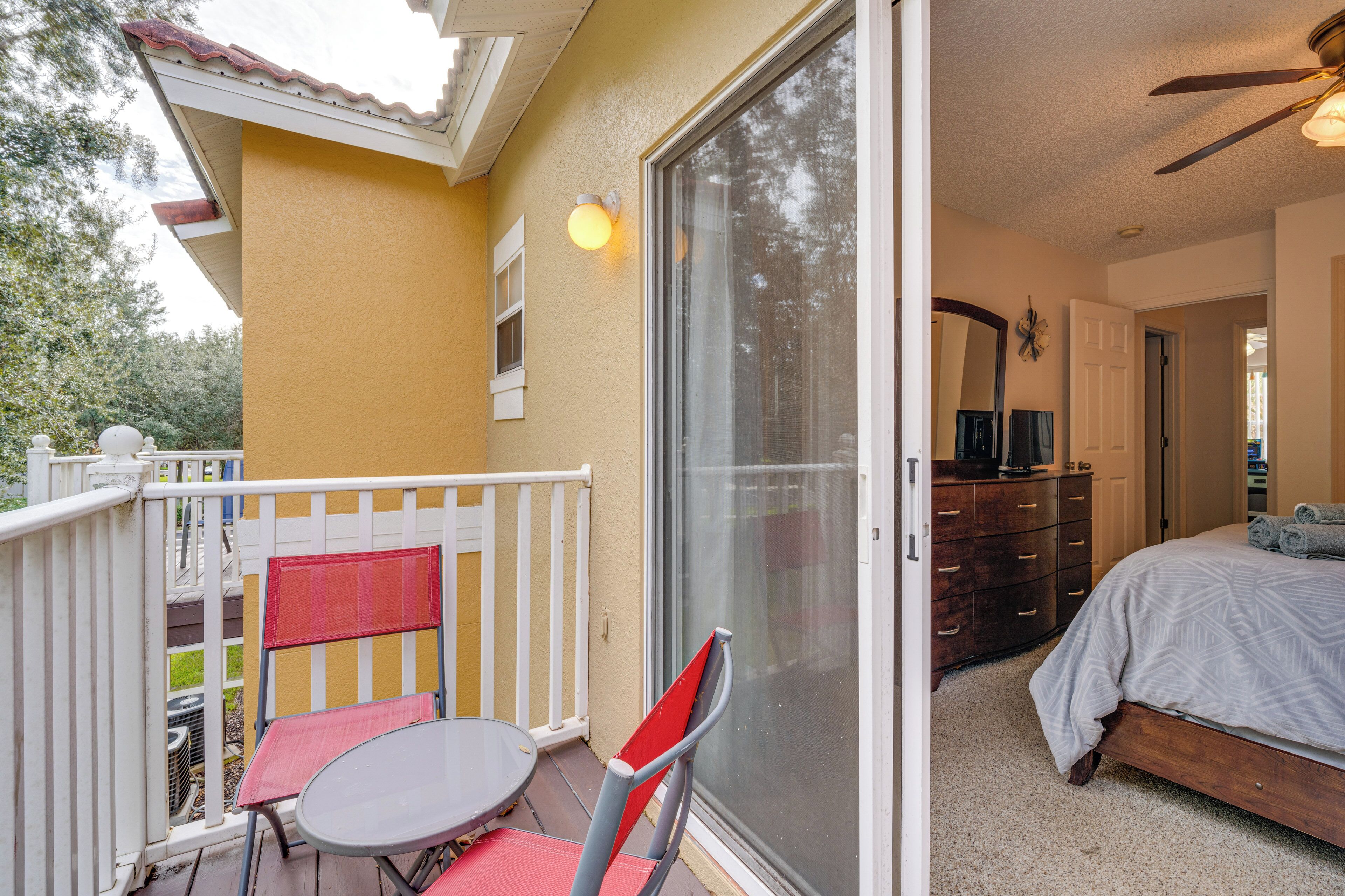Ein Balkon mit Tisch und Stühlen, eine Glasschiebetür, die zu einem Schlafzimmer mit Bett und Kommode führt.