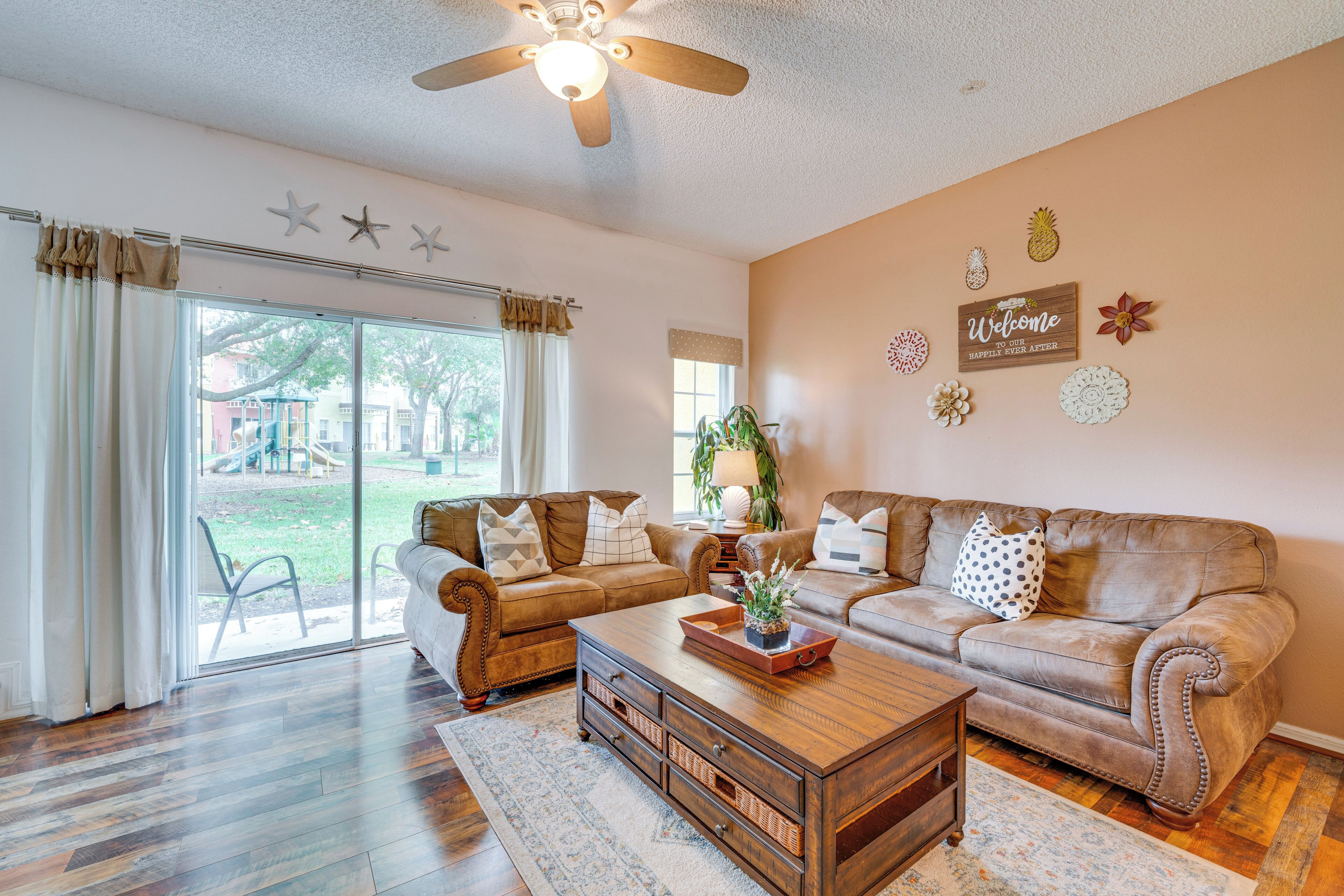 A spacious living room with two leather sofas, a wooden coffee table, and a large sliding glass door leading to a backyard.