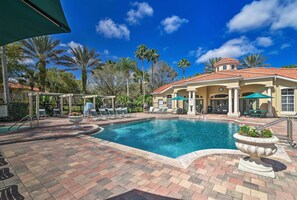 A swimming pool area with lounge chairs, a covered seating area, and a building with a tiled roof.