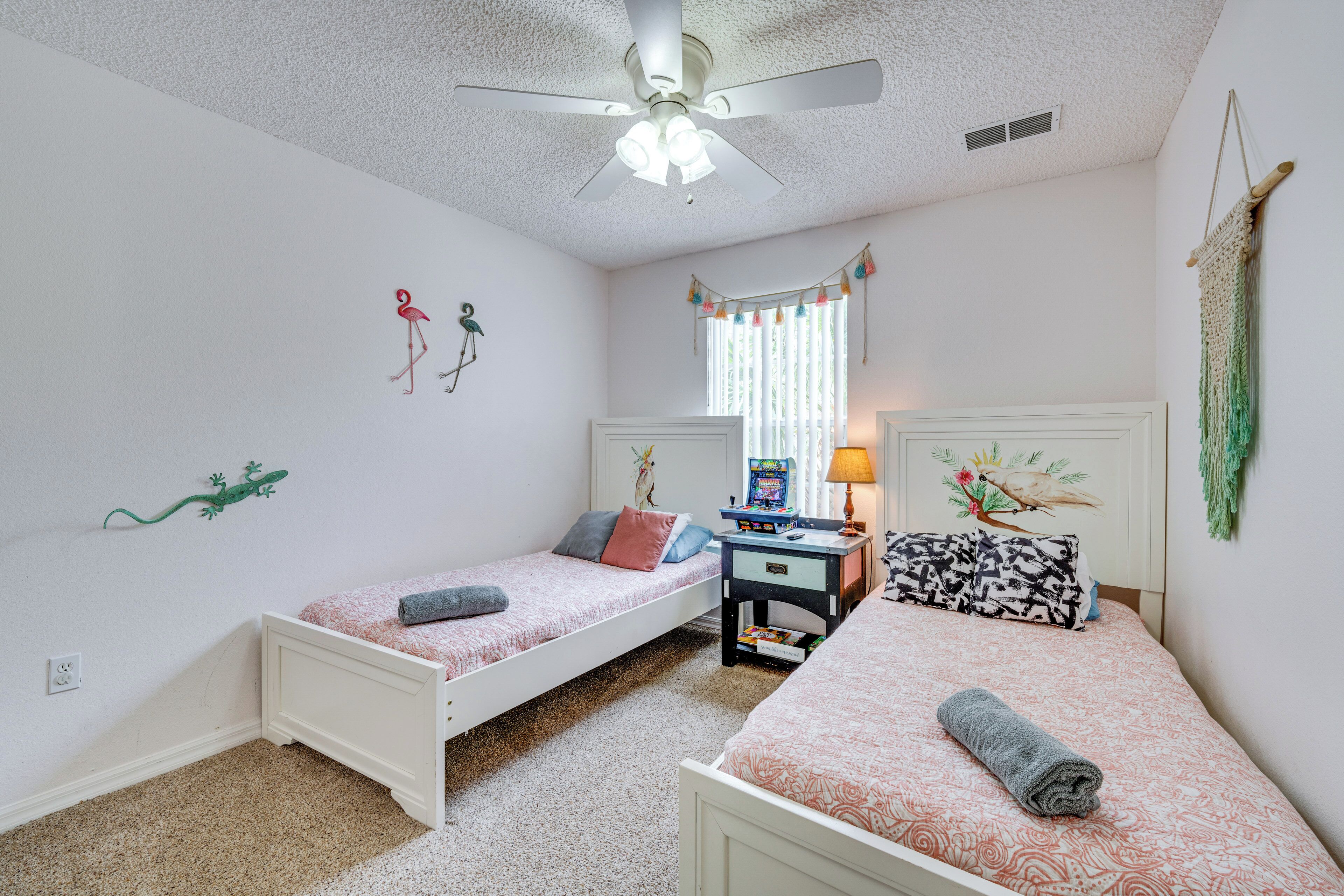 A bedroom with two single beds, a ceiling fan, a window with curtains, and a desk with a lamp.