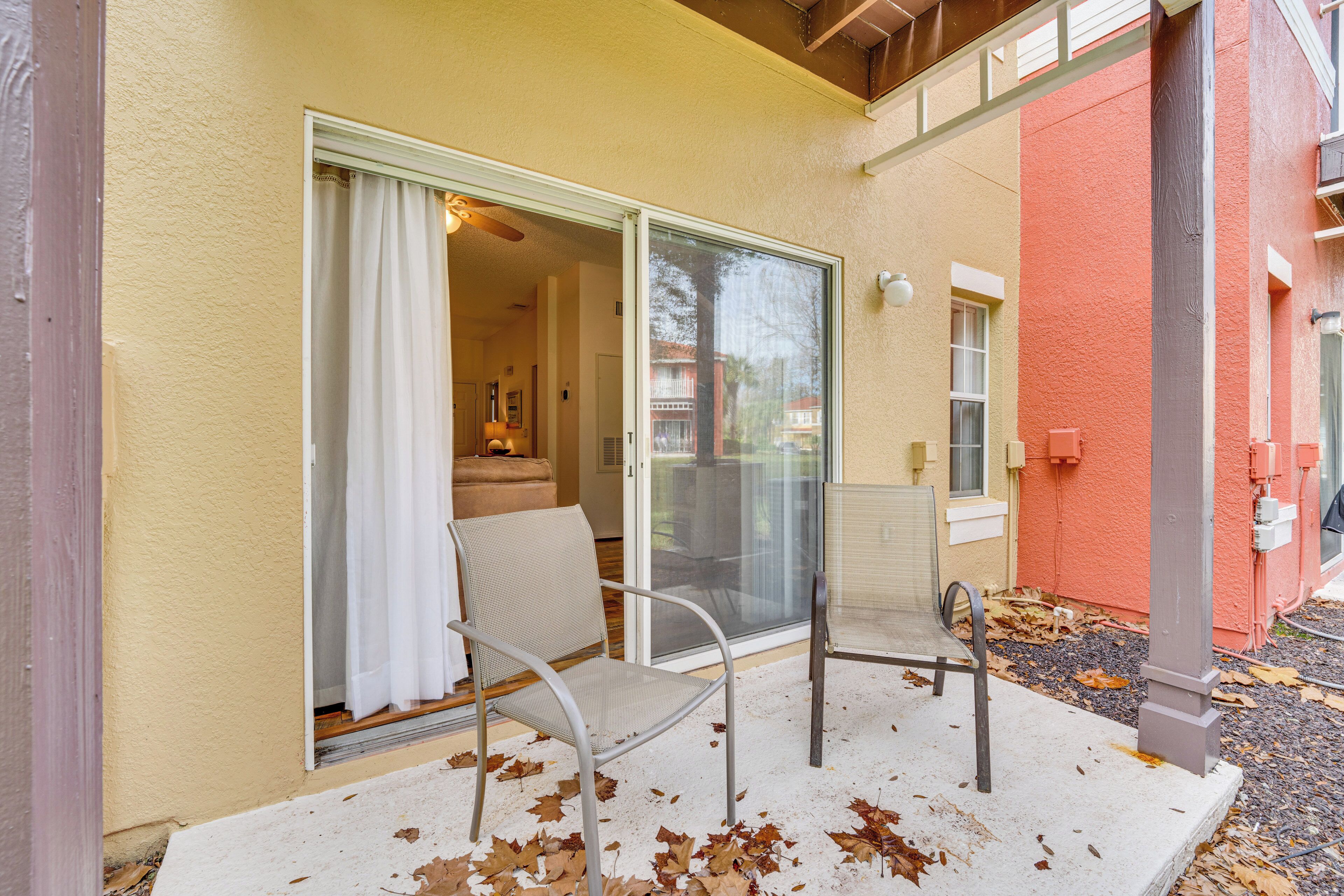 Eine Terrasse mit einer Schiebetür zu einem Raum, einem Metallstuhl und einem Betonboden mit verstreuten Blättern.