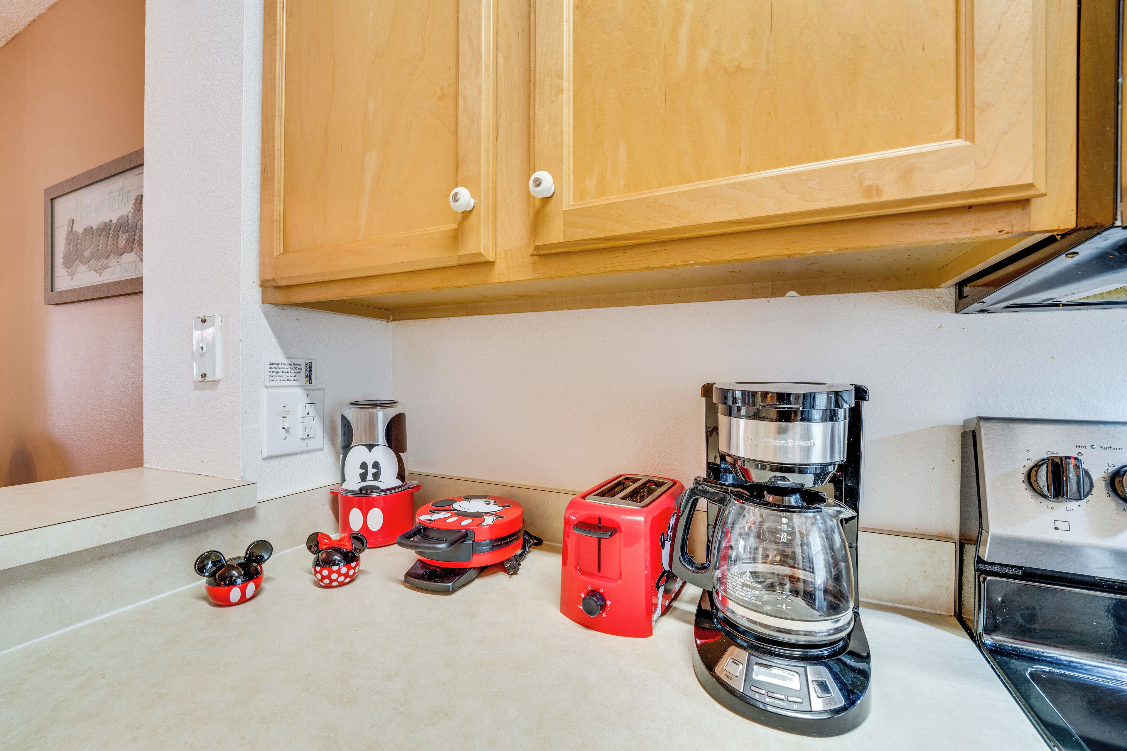 A kitchen with wooden cabinets, a coffee maker, a toaster, and Mickey Mouse-themed kitchenware.
