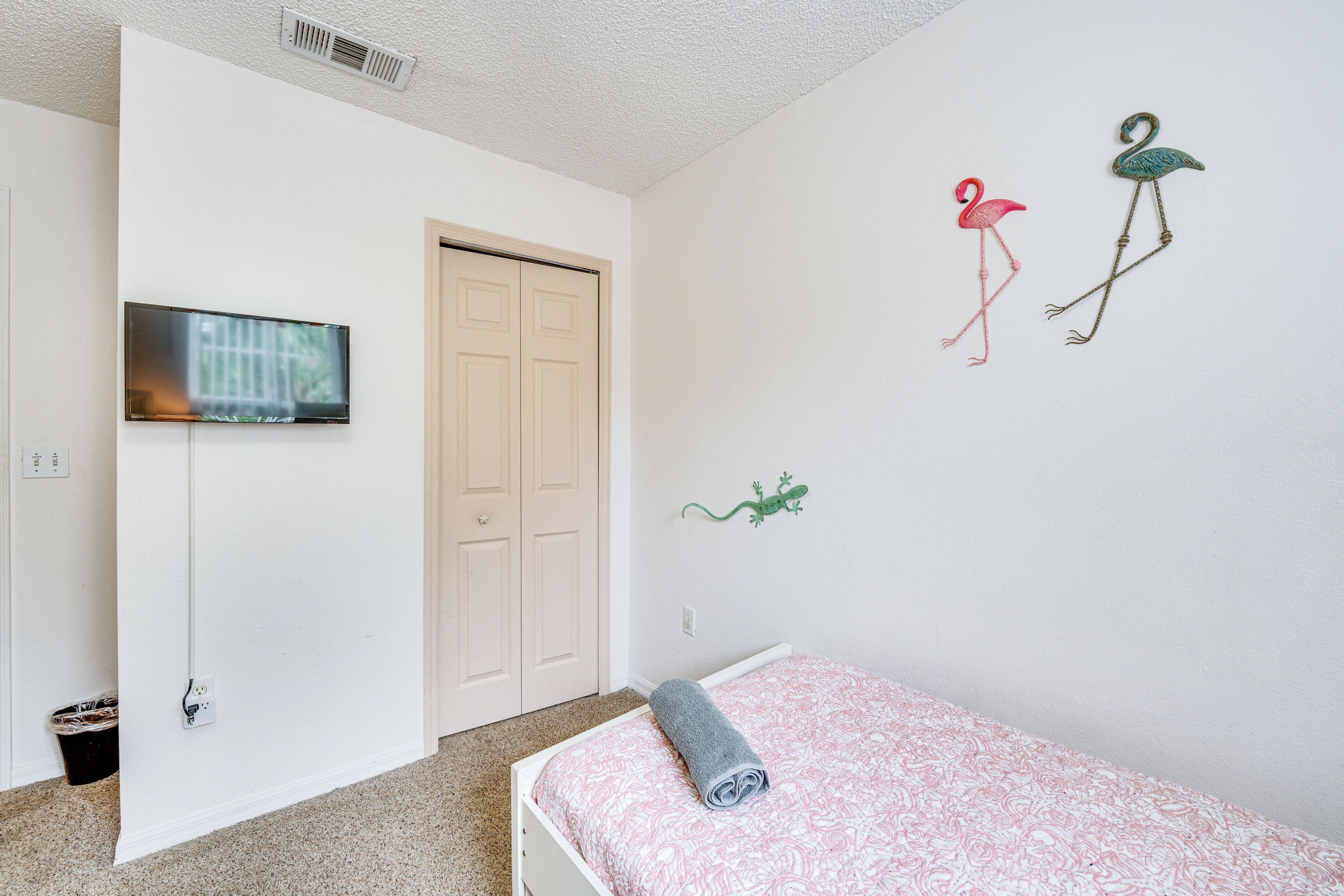 Un dormitorio con una cama, televisión montada en la pared y una puerta.