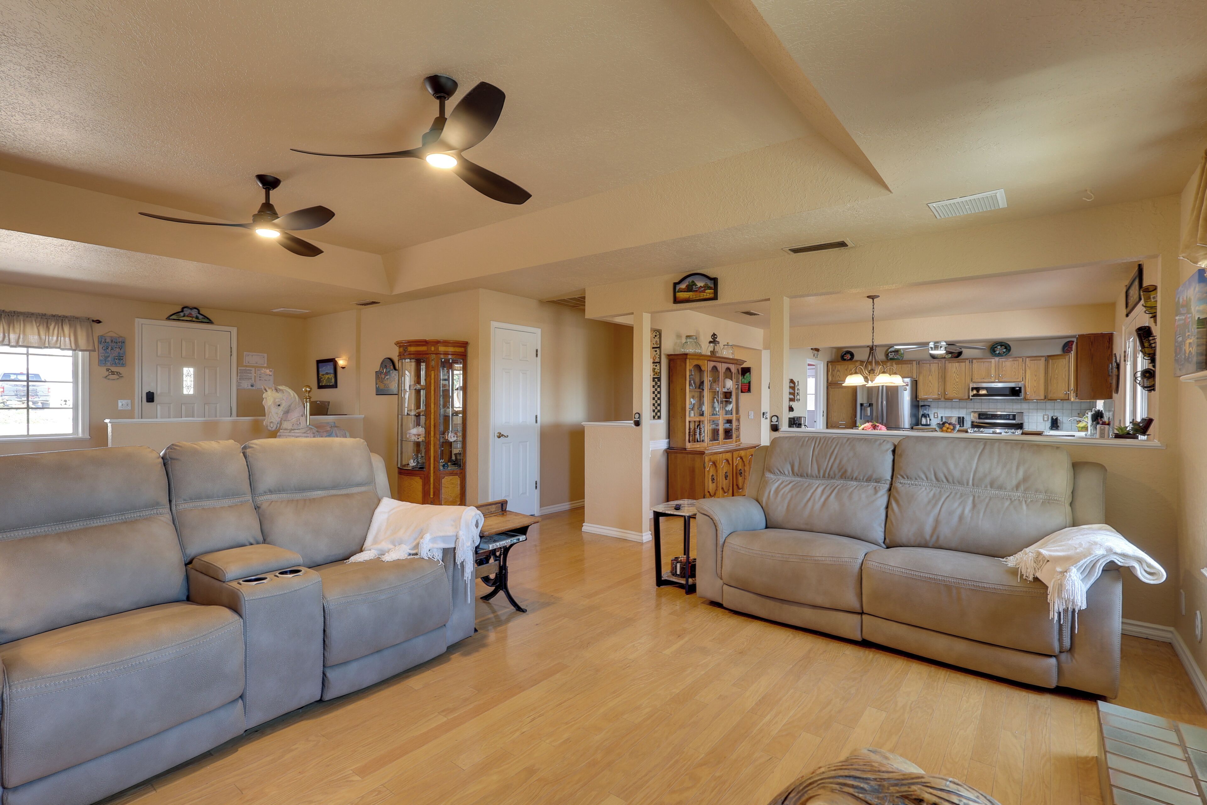 A spacious living room with a beige sofa, a dining area with a kitchen in the background, and a ceiling fan.