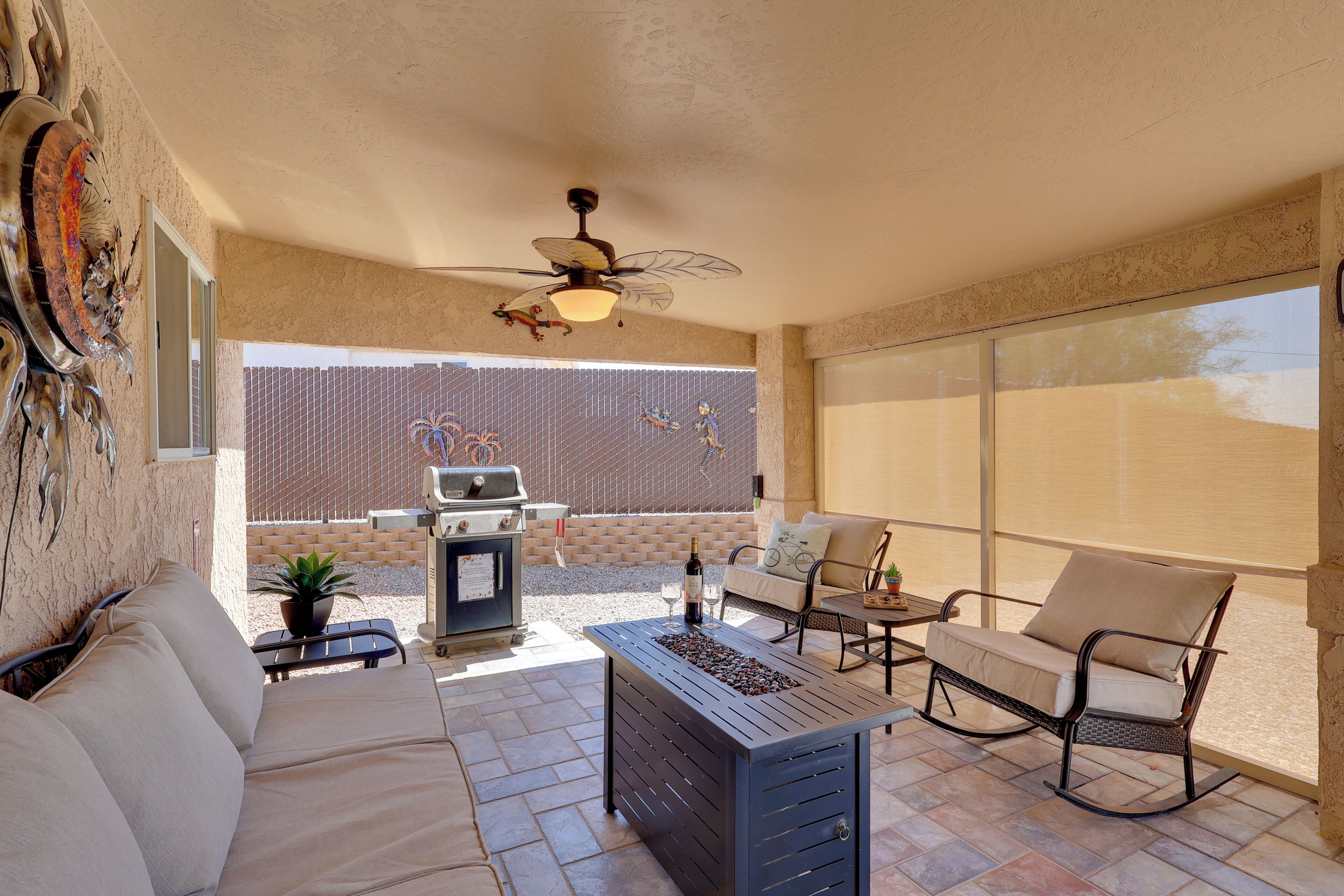 A patio area with a ceiling fan, a grill, a sofa, and a table with a bottle and glasses.