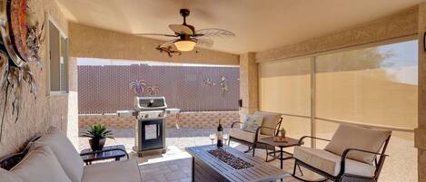 A patio area with a ceiling fan, a grill, a sofa, and a table with a bottle and glasses.