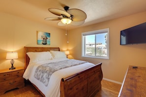 A bedroom with a wooden bed, a ceiling fan, a TV, a window with a view, and a nightstand with a lamp. - Furnished Patio, Grill & Views: Lake Havasu Home (Lake Havasu City)