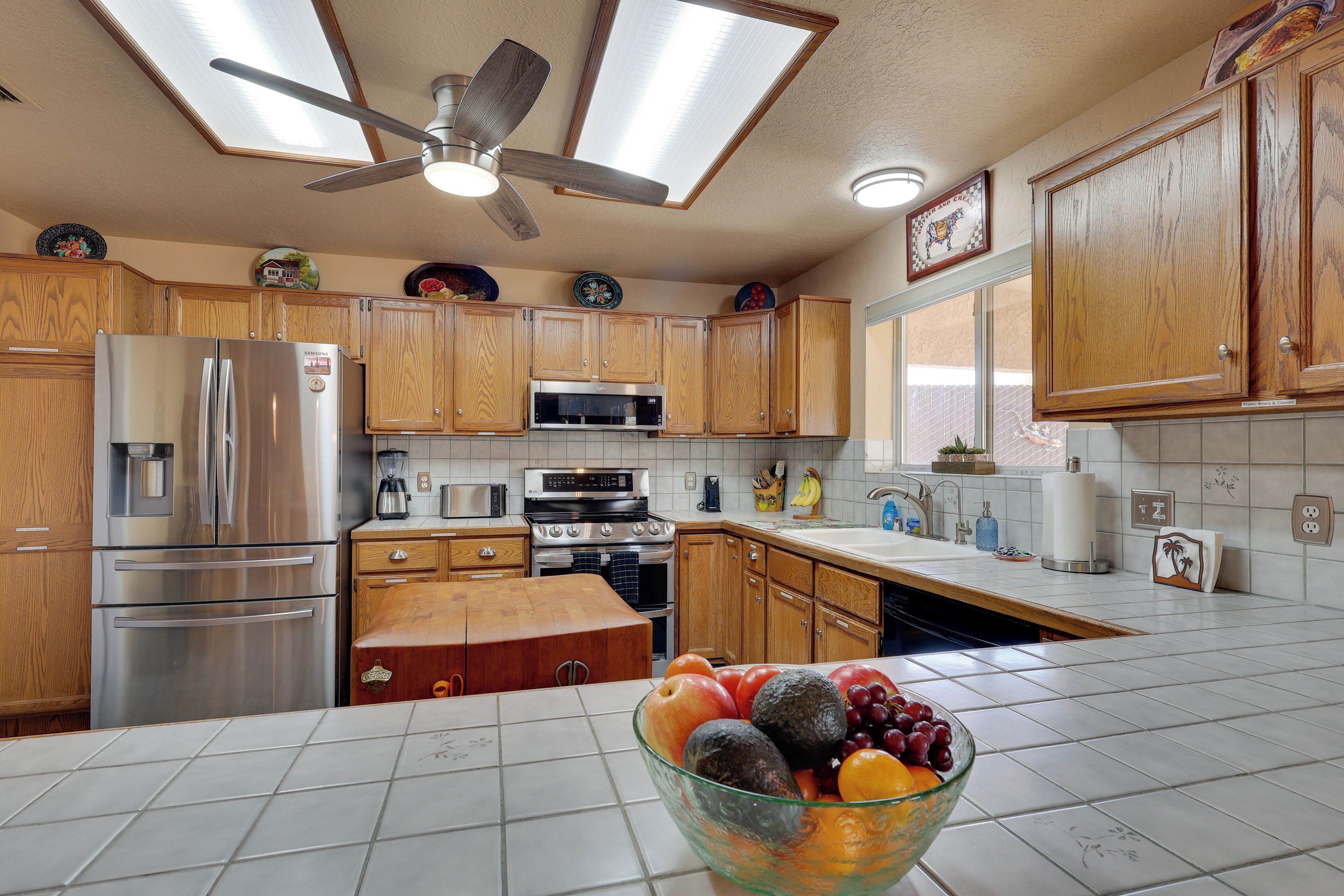 A kitchen with wooden cabinets, stainless steel appliances, a ceiling fan, and a bowl of fruit on the counter.