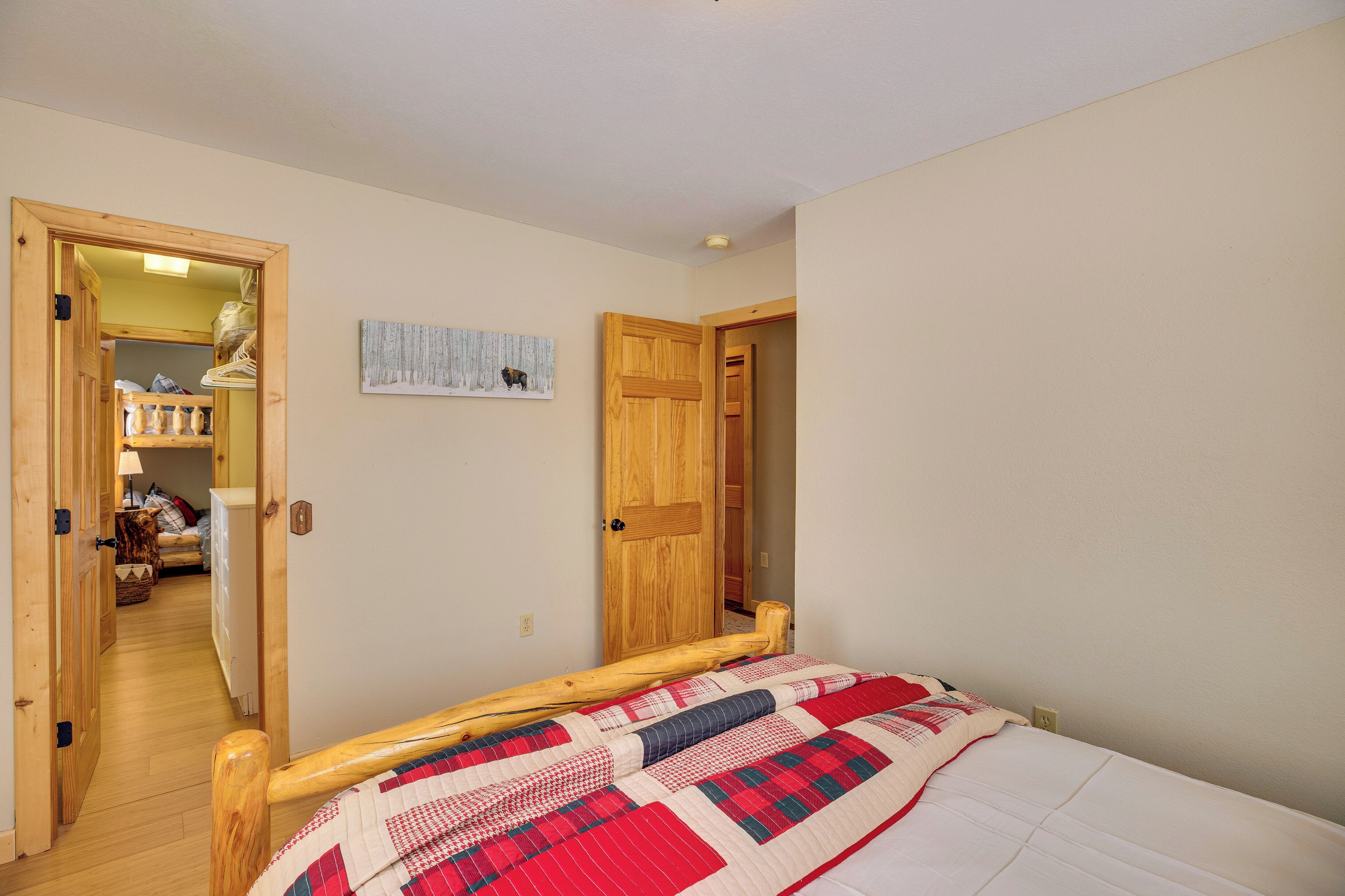 Une chambre à coucher avec un cadre de lit en bois, une courtepointe et une porte donnant sur un couloir où se trouvent un radiateur et un lit.