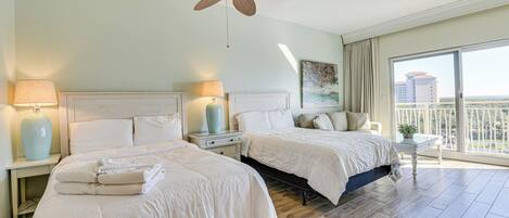 Une chambre d’hôtel avec deux lits, un ventilateur de plafond, une grande fenêtre donnant sur un beau paysage et une table de chevet avec une lampe.