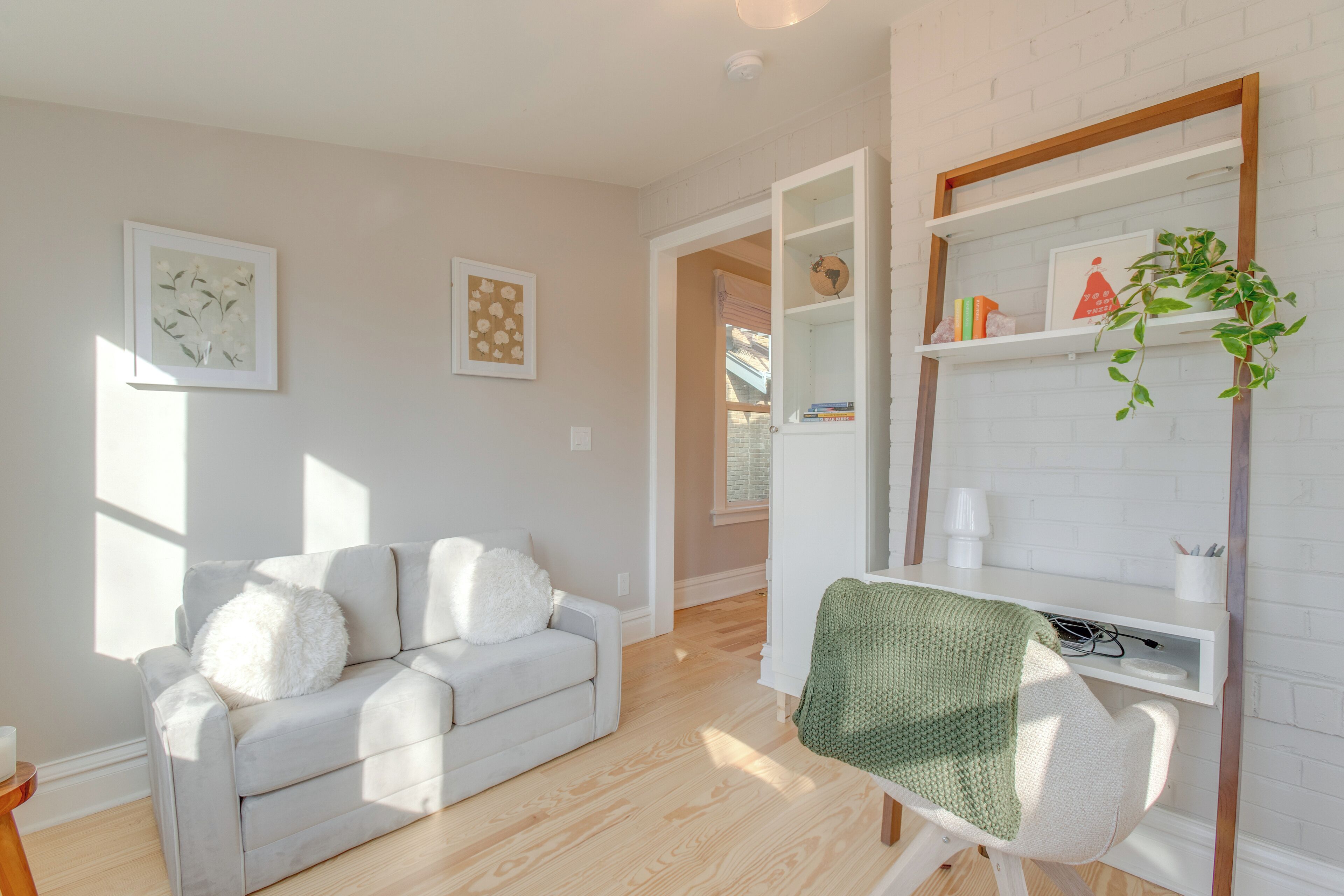 A modern living room with a light-colored sofa, a green chair, and a white desk with shelves.