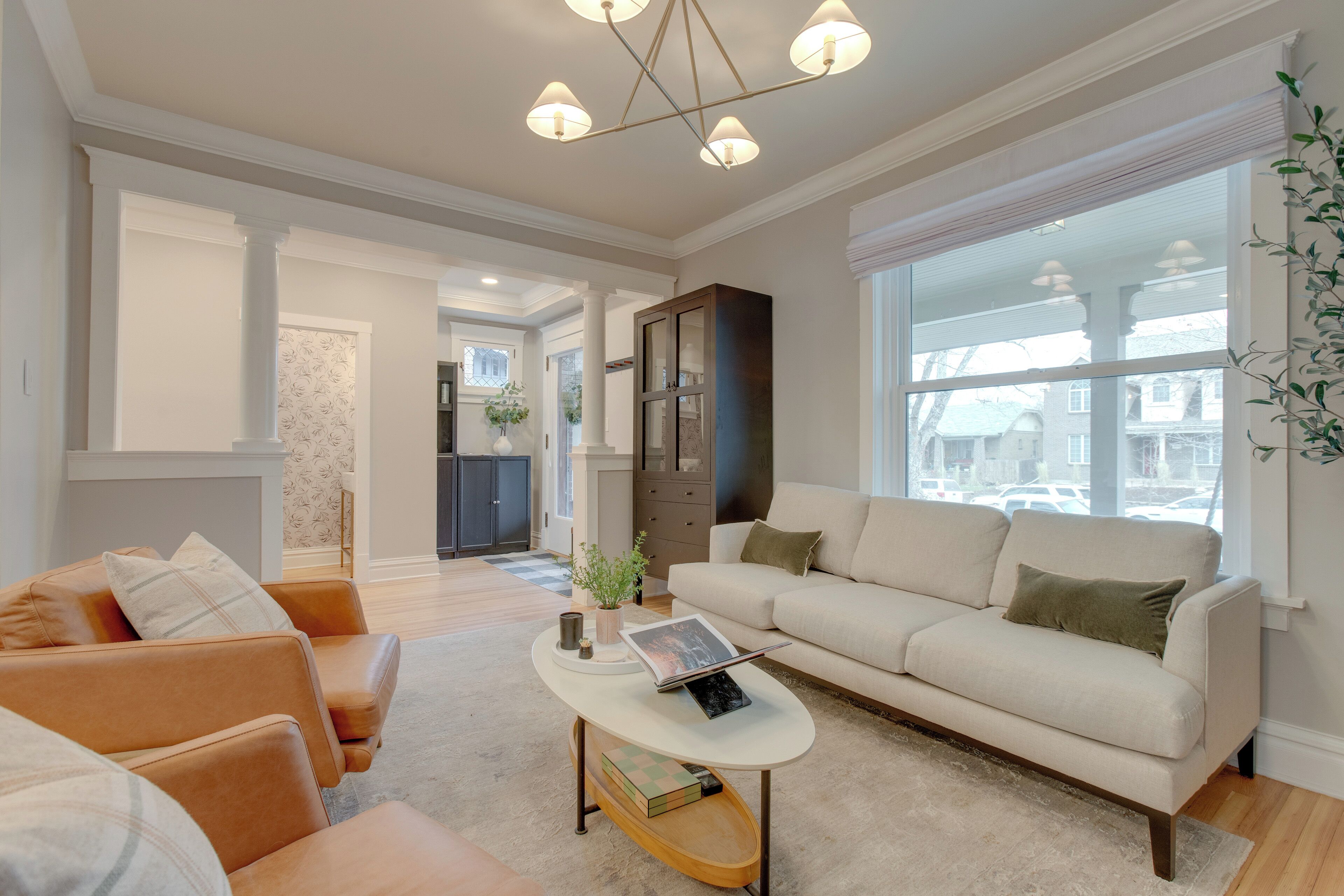 En rummelig stue med en beige sofa, et sofabord og et stort vindue med udsigt til gaden.