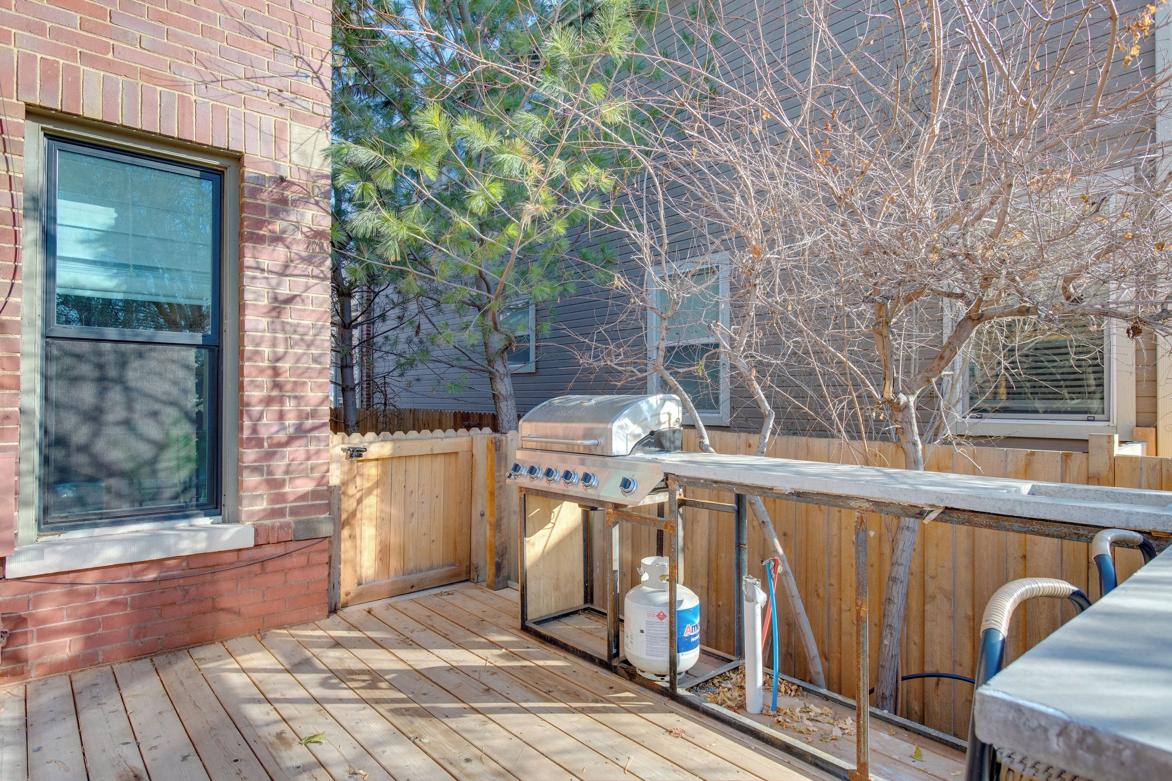 A wooden deck with a barbecue grill and propane tank, a brick building, and a tree.