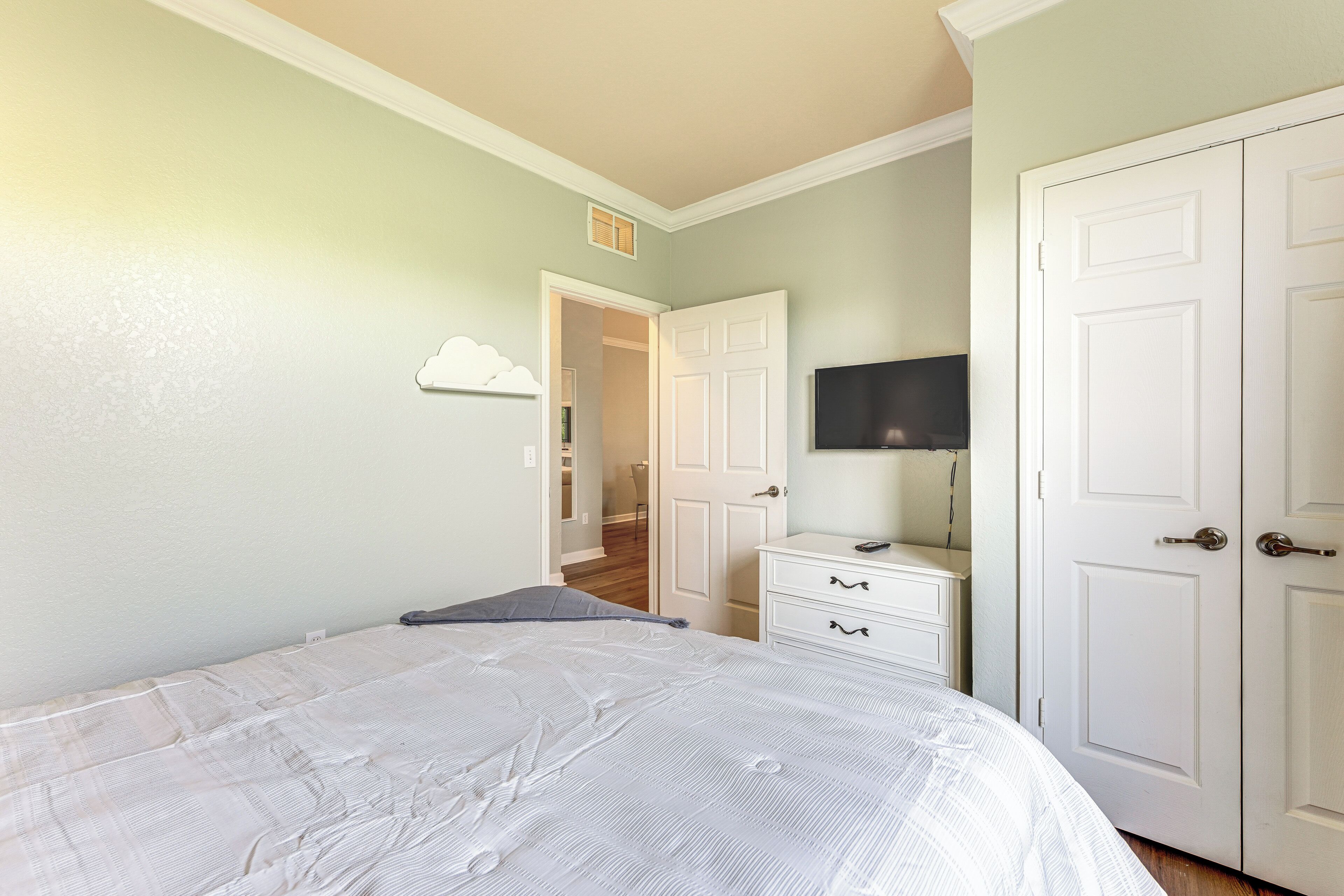A bedroom with a bed, a dresser, a TV on a stand, and a closet.
