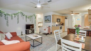 A modern living room with a sofa, coffee table, and a dining area with chairs and a table. There is a kitchen area with cabinets and appliances.