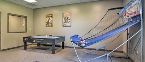 A room with a pool table, a basketball hoop, and posters on the wall.