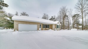 A two-story house with a garage, surrounded by snow-covered ground and trees. - Cozy Mancelona Home: Ski, Golf & Snowmobile! (Mancelona)