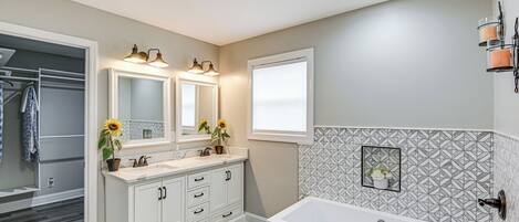 A bathroom with a double sink vanity, a bathtub, and a mirror with lights.