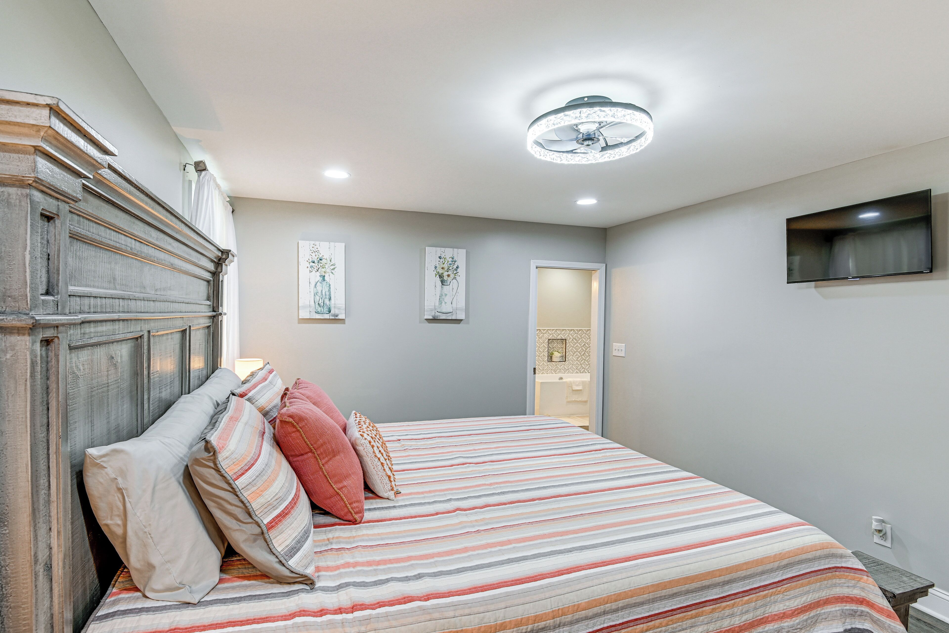 A bedroom with a bed, a wooden headboard, a ceiling fan, and a TV mounted on the wall.