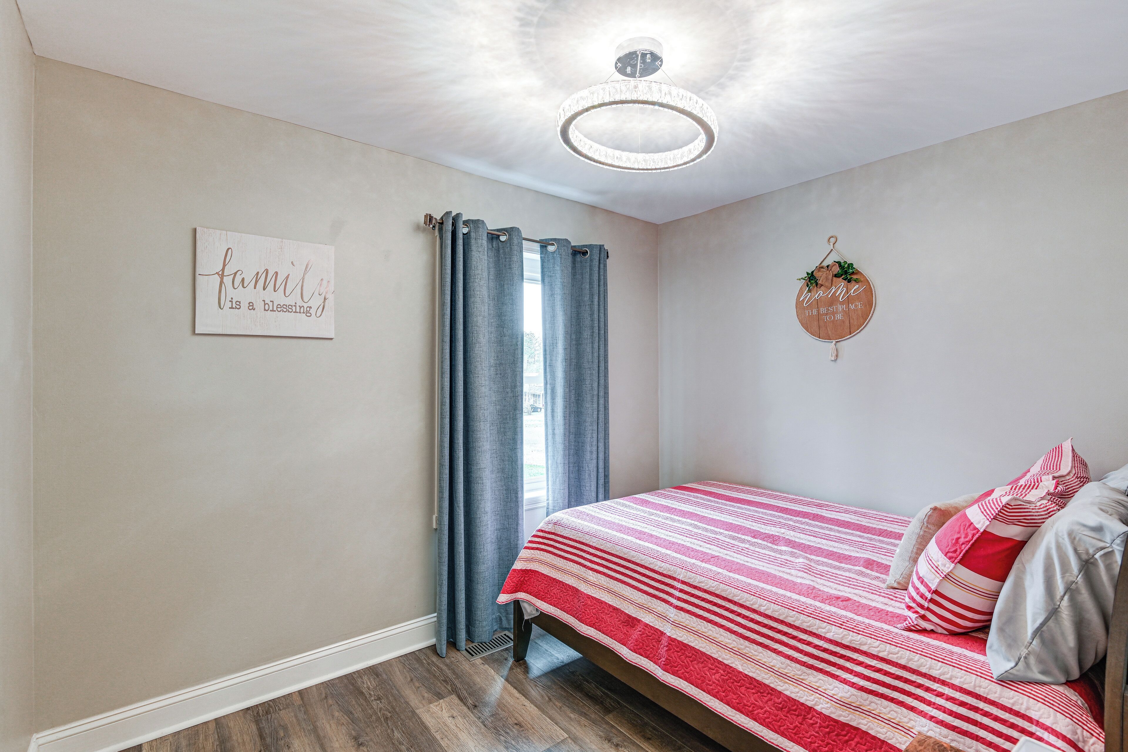 A bedroom with a bed, curtains, a chandelier, a wall sign, and a window.