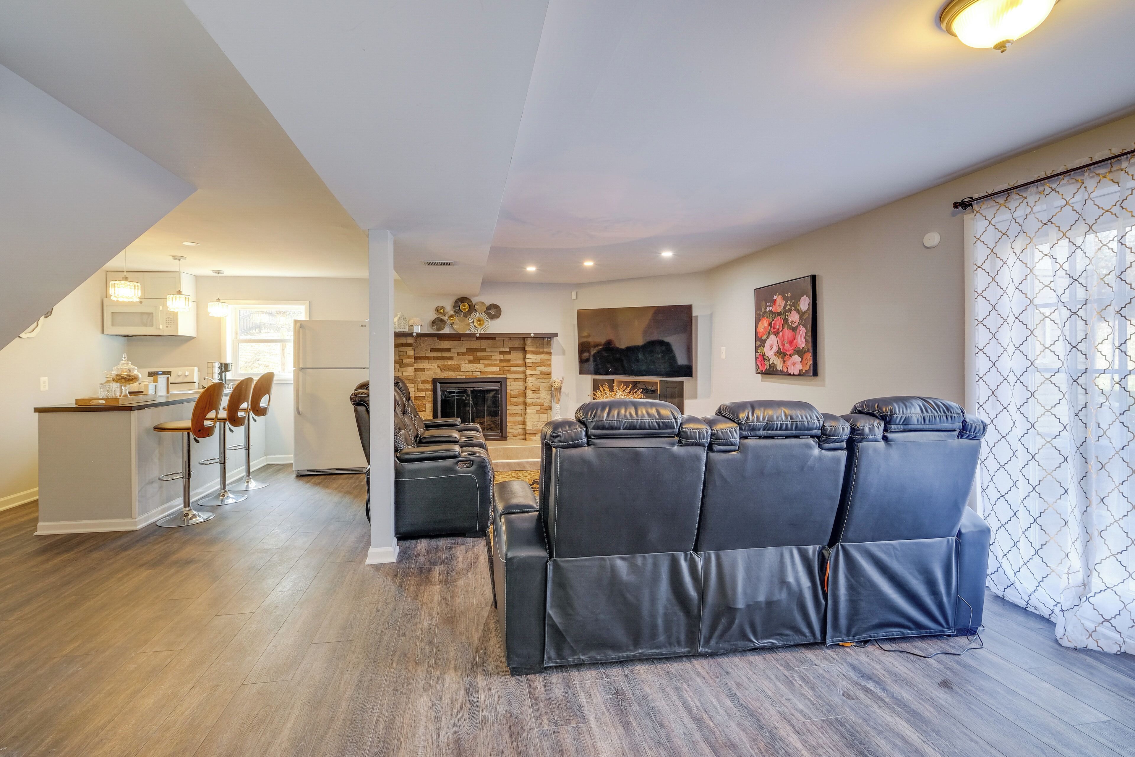 A modern living room with a black leather sofa, a kitchen area with a microwave and bar stools, and a fireplace.