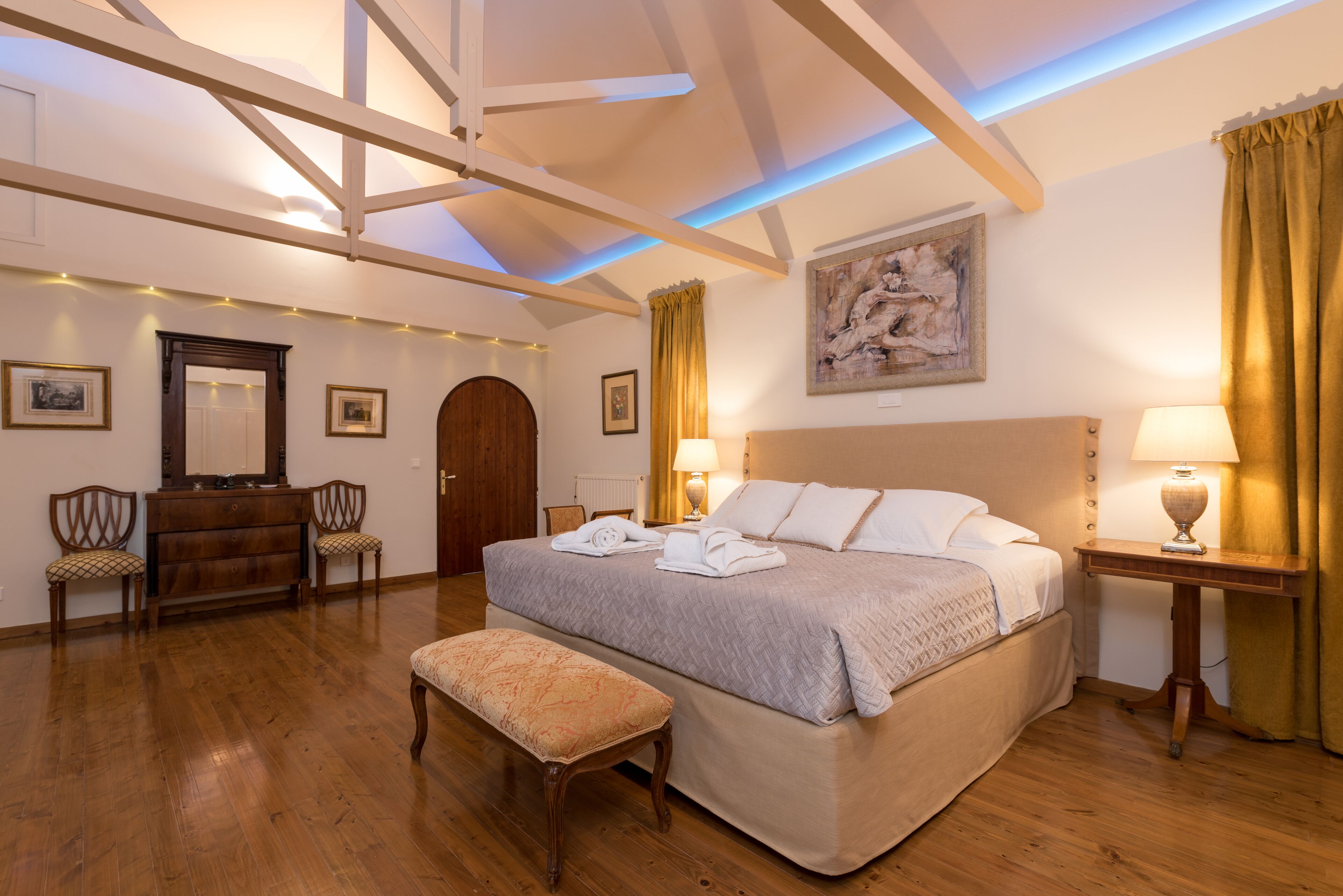 A spacious bedroom with a large bed, wooden floor, and a ceiling with exposed beams.