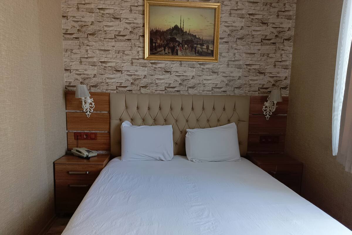 A hotel room with a large bed, a headboard with a tufted design, two bedside tables with lamps, a wall-mounted painting, and a textured wall.