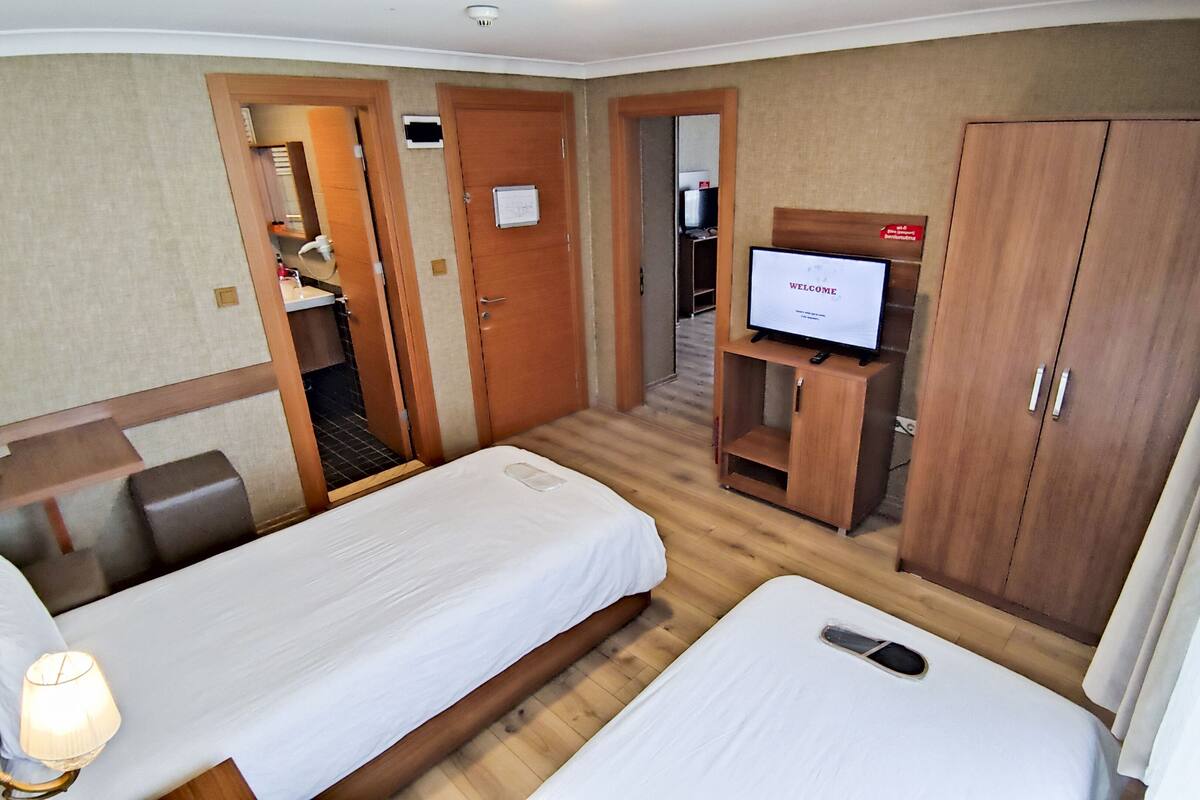 A hotel room with two beds, a TV, wooden wardrobe, and a small desk with a lamp.