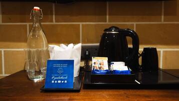Una encimera de cocina con una cafetera, sobres de azúcar, una botella de vidrio y un portavasos.
