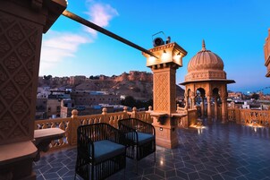 A terrace with a view of a historic fort, a small pavilion, and a dining area with chairs and tables.