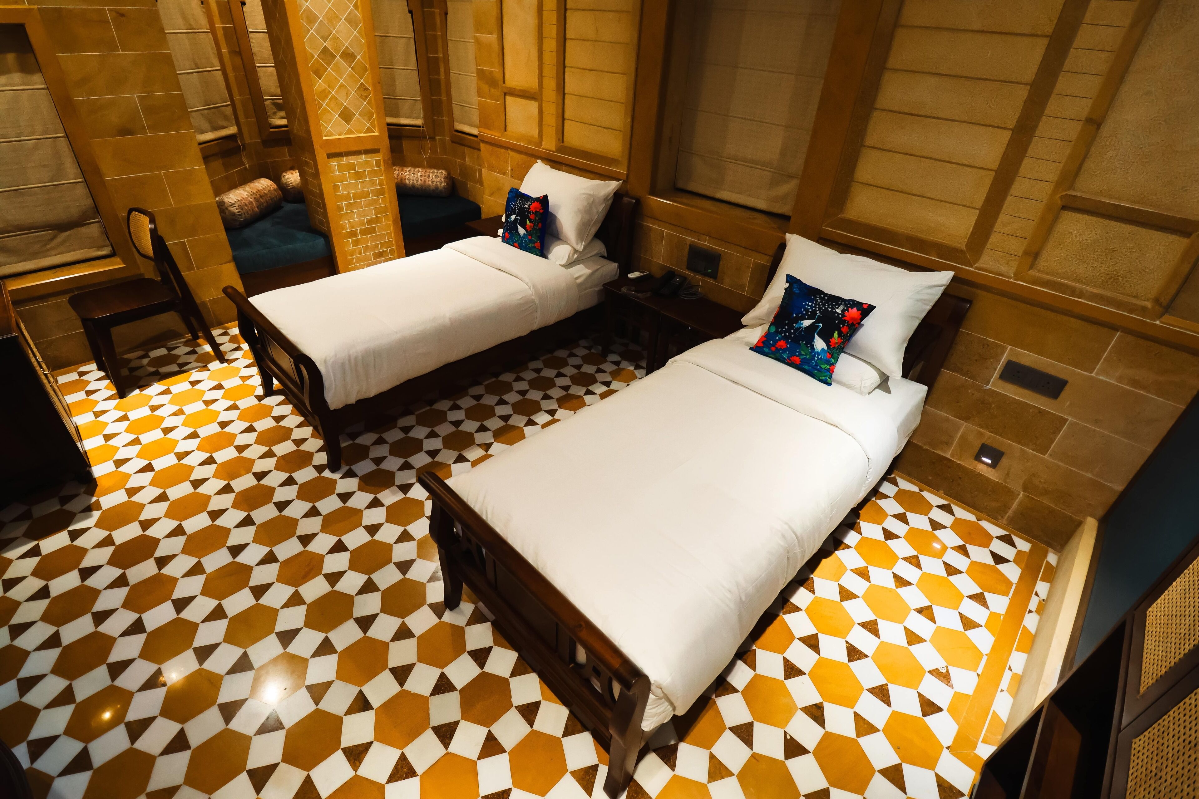 Una habitación con dos camas, suelo de baldosas a cuadros, cabeceros de madera y un pequeño escritorio con silla.