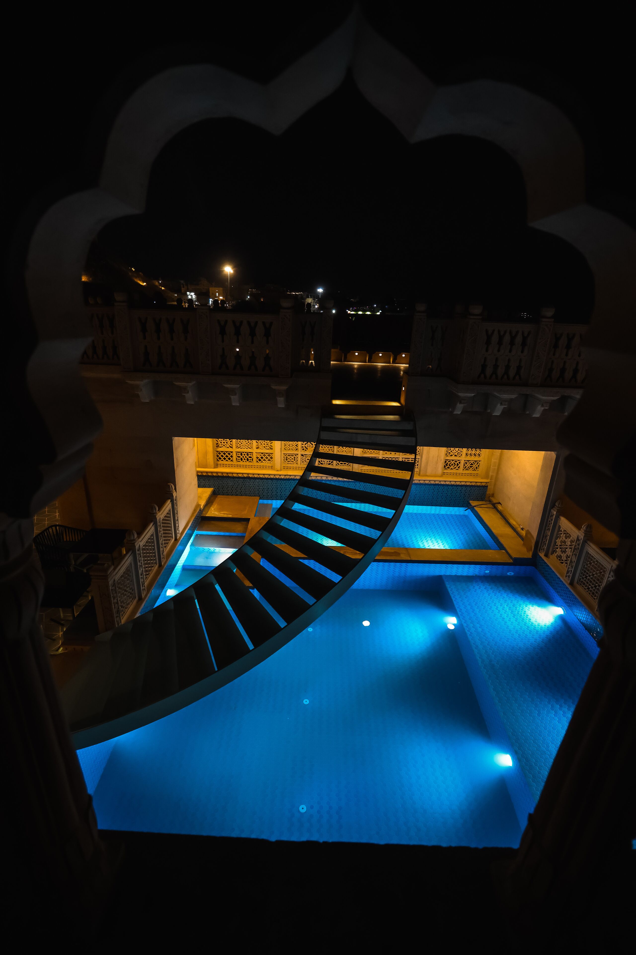 Una piscina con iluminación azul, rodeada por una zona decorativa junto a la piscina con paredes y barandillas con diseños.