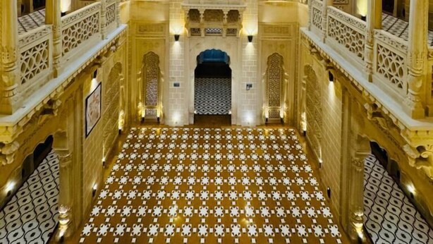 A grand hall with intricate ceiling artwork and a patterned floor, featuring symmetrical arches and detailed wall carvings.
