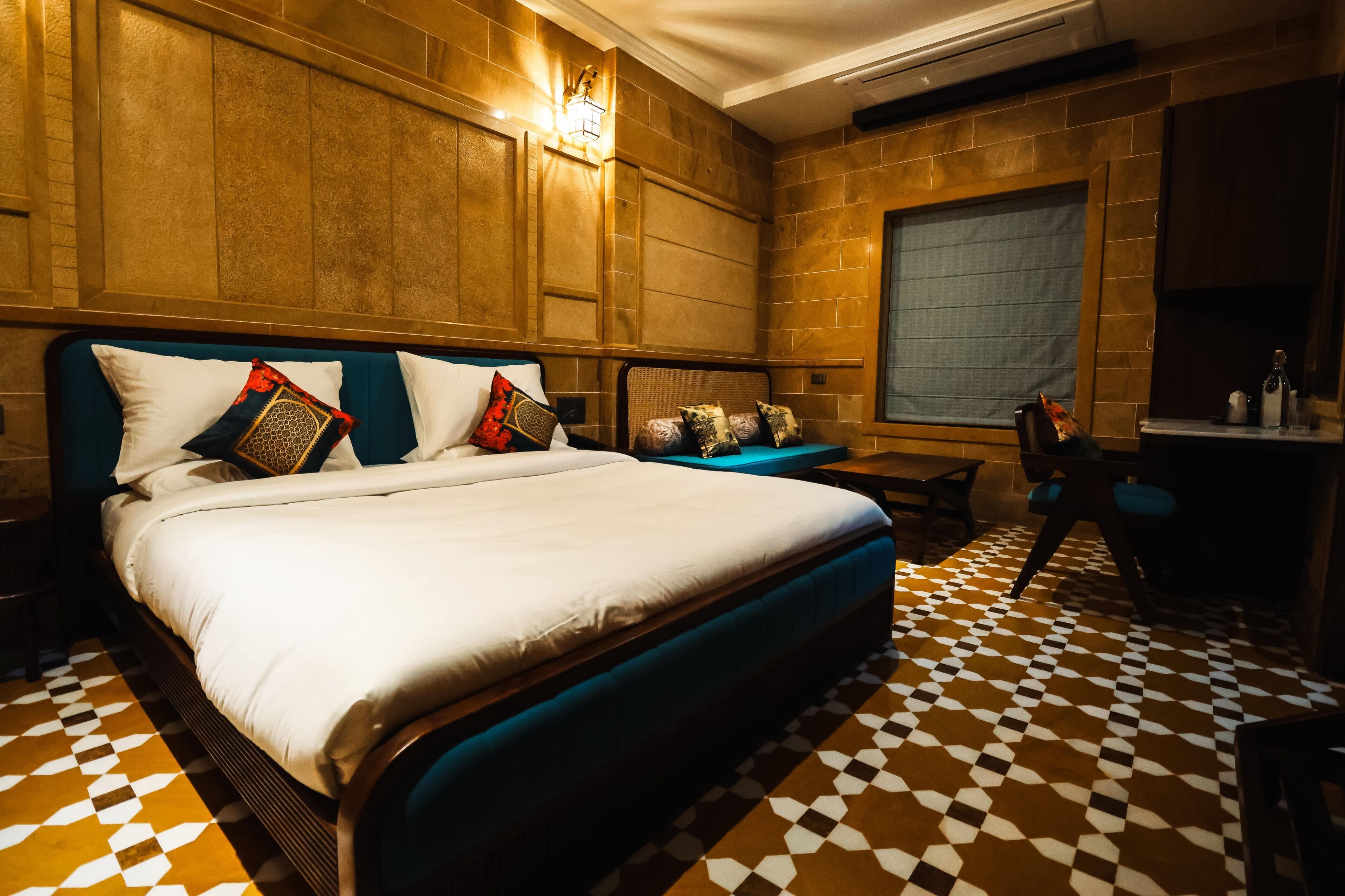 Ein Hotelzimmer mit einem großen Bett, einem Schreibtisch und einem Stuhl. Der Raum hat einen Schachbrettboden und Holzvertäfelung.