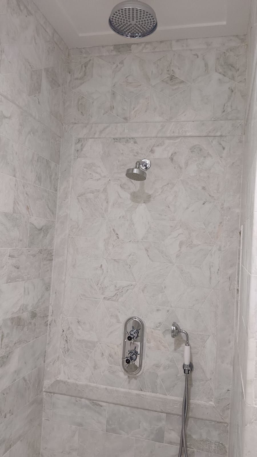 A shower area with a rain showerhead, handheld showerhead, and a handheld shower attachment.