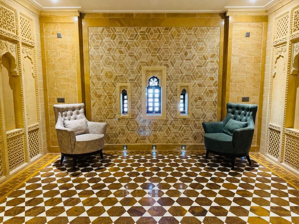 A room with a checkered floor, two armchairs, and a patterned wall with three small windows.