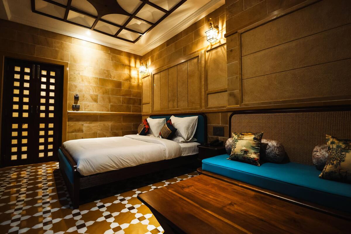 Ein Hotelzimmer mit Schachbrettmuster-Boden, einem Bett mit weißer Bettwäsche, einem blauen Sofa und einem Holztisch.