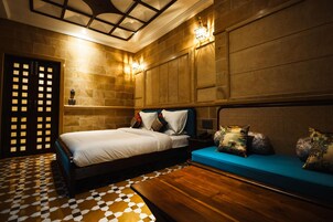 A hotel room with a checkered floor, a bed with white linens, a blue sofa, and a wooden coffee table.