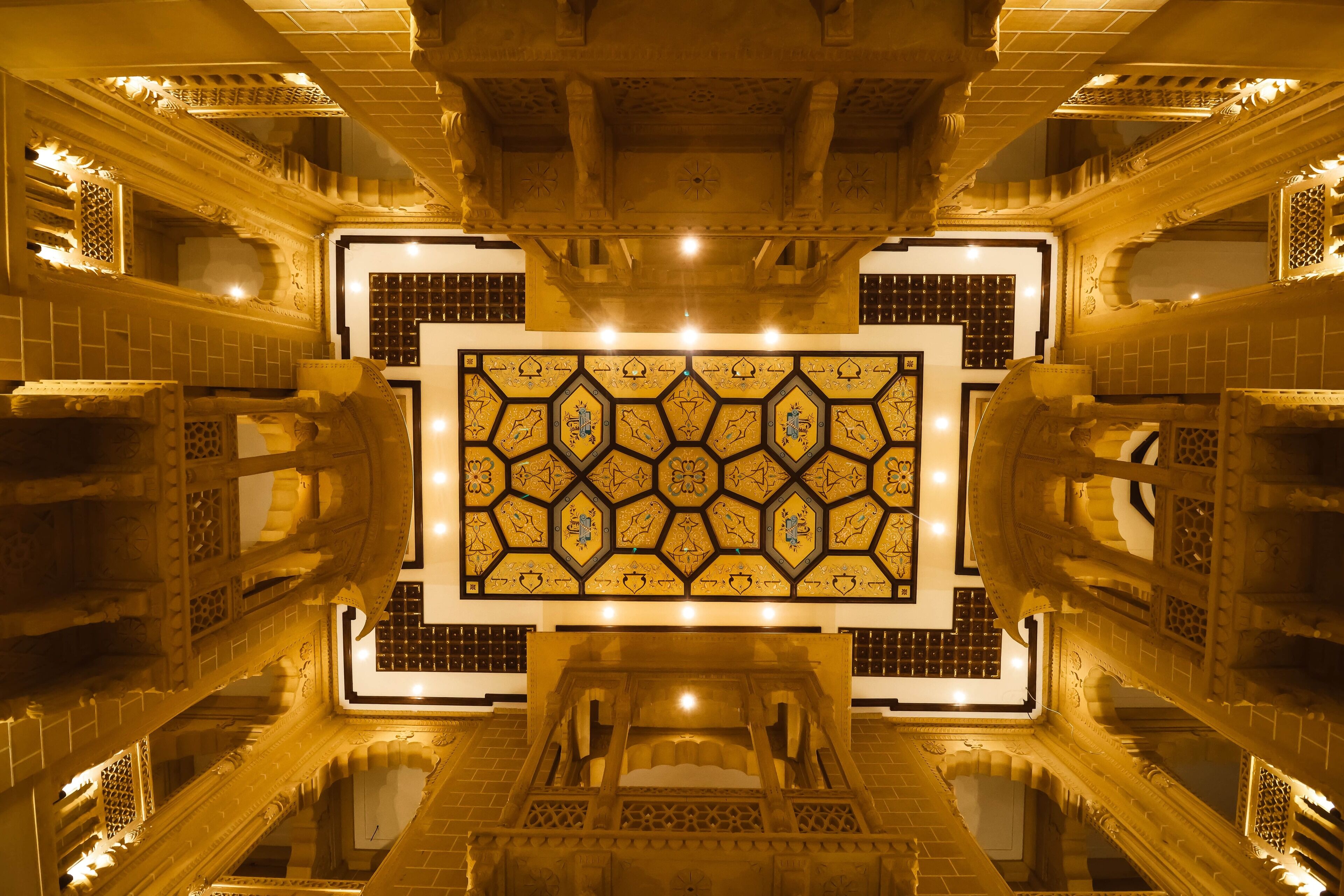 An ornate interior with a central geometric patterned wall, intricate ceiling designs, and reflective flooring.