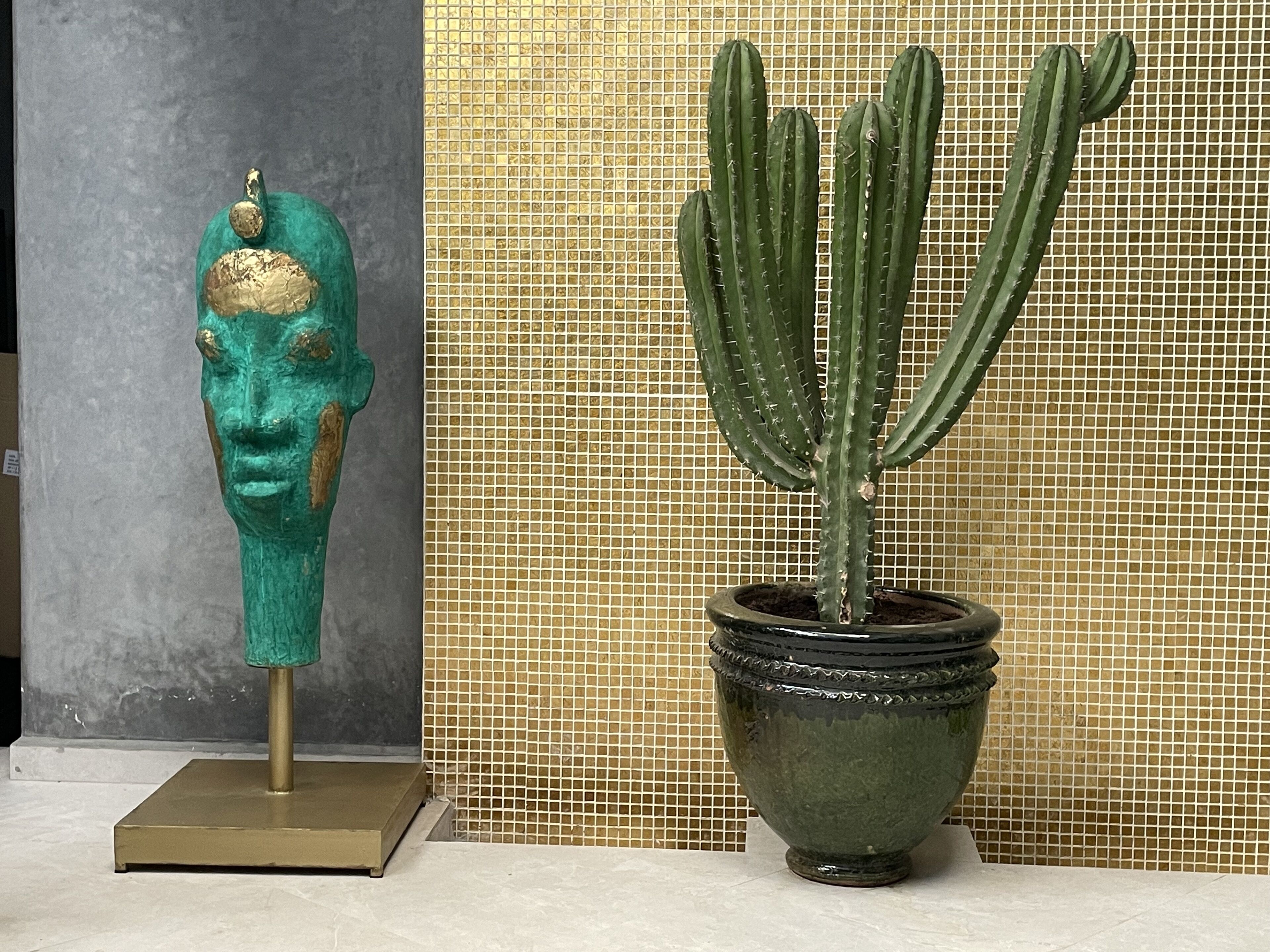 Un cactus en maceta y una escultura de busto sobre un suelo de baldosas.