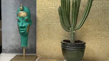 Un cactus en maceta y una escultura de busto sobre un suelo de baldosas.
