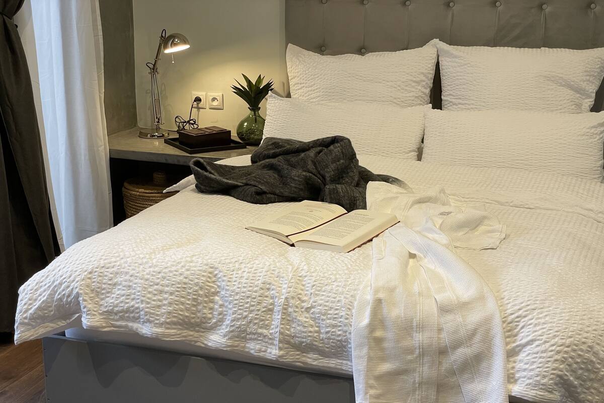 A neatly made bed with a white textured duvet, a book, and a blanket on it.