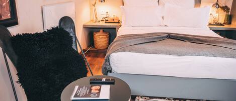 A neatly arranged bedroom with a bed, a chair, a small table with a book, and a bedside lamp.